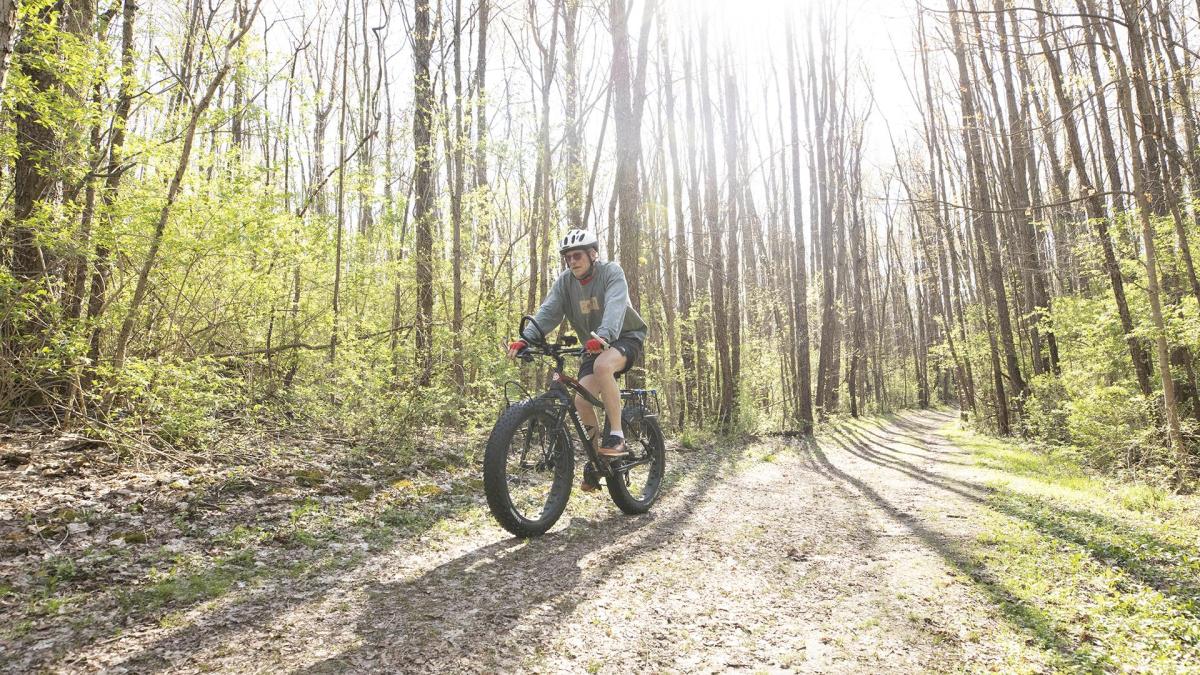 A man biking on a trail through Love Creek County Park, surrounded by trees and natural scenery on a peaceful day