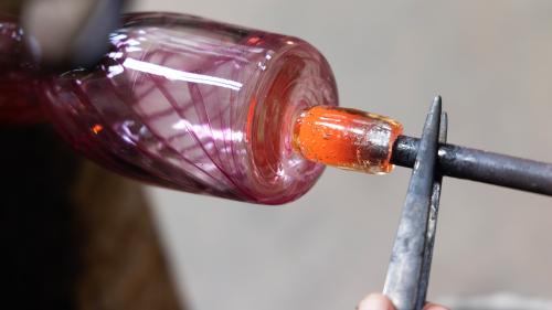 A detailed shot of a glassblowing creation in progress at Water Street Glassworks, showcasing swirling colors of purple, orange, and clear glass