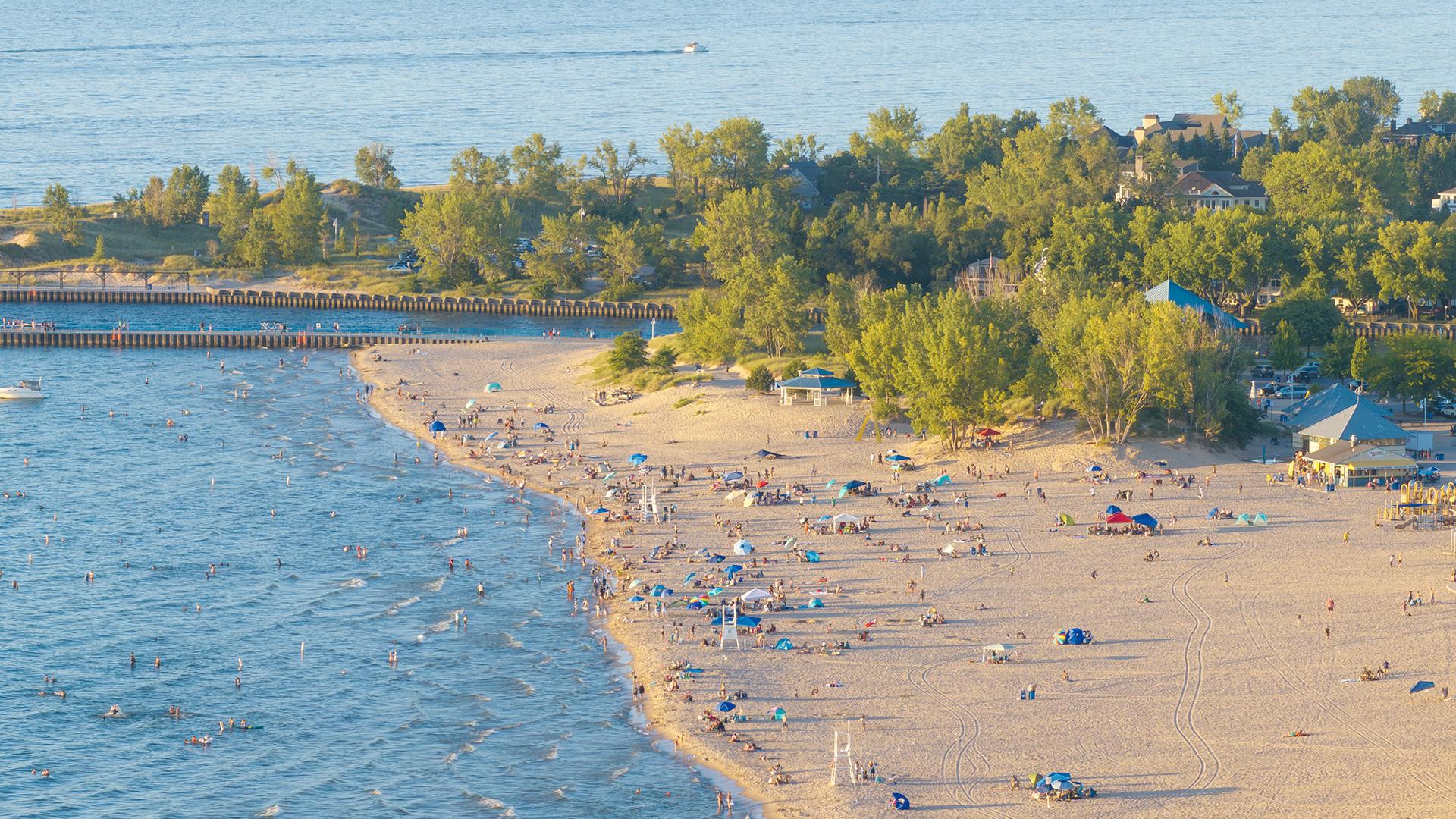 A drone shot of Silver Beach on a sunny summer day, with groups of people scattered along the shore enjoying the beach, swimming, and relaxing in the sun