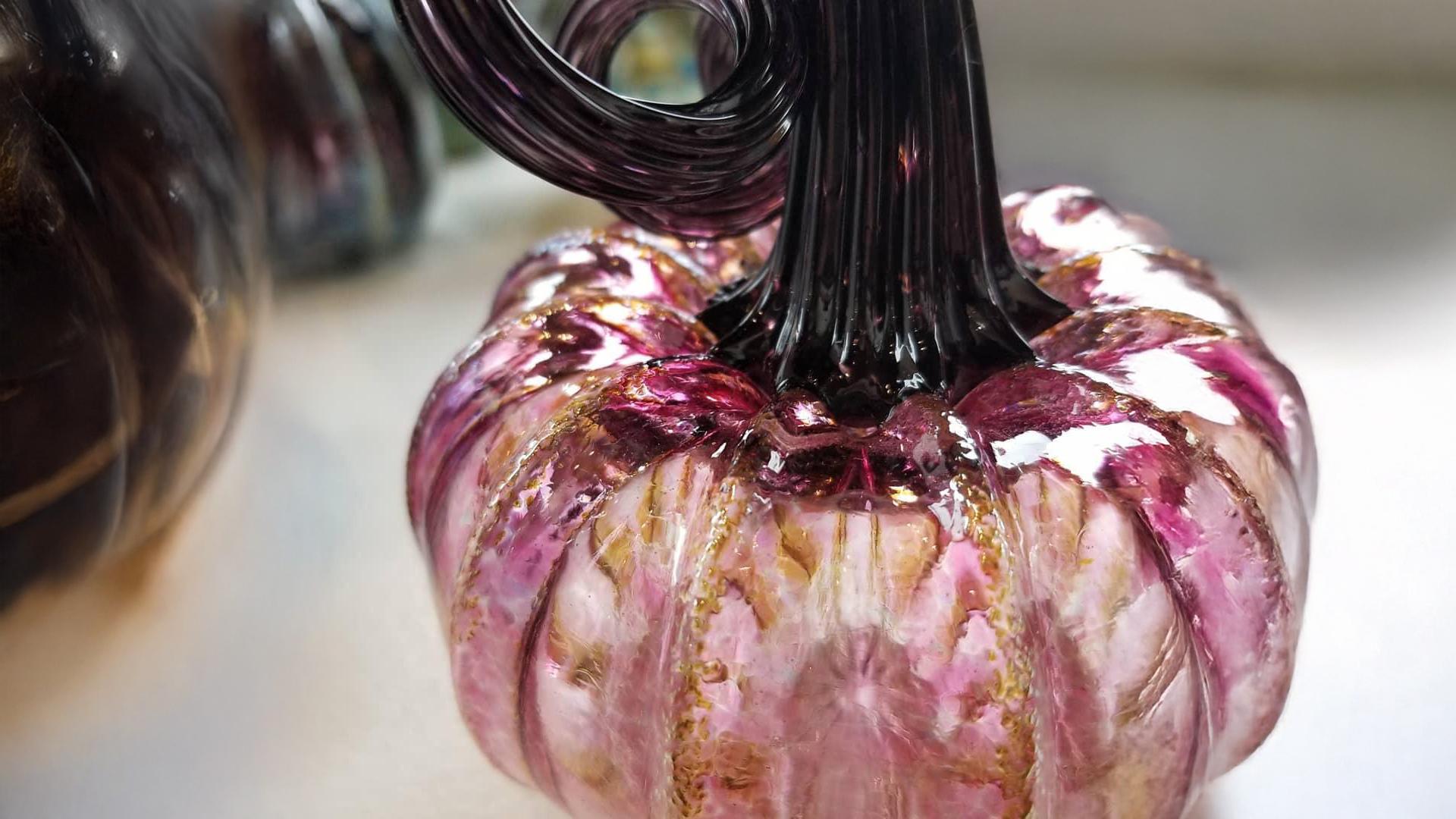 A close-up of a decorative glass pumpkin at Water Street Glassworks with pink and gold hues