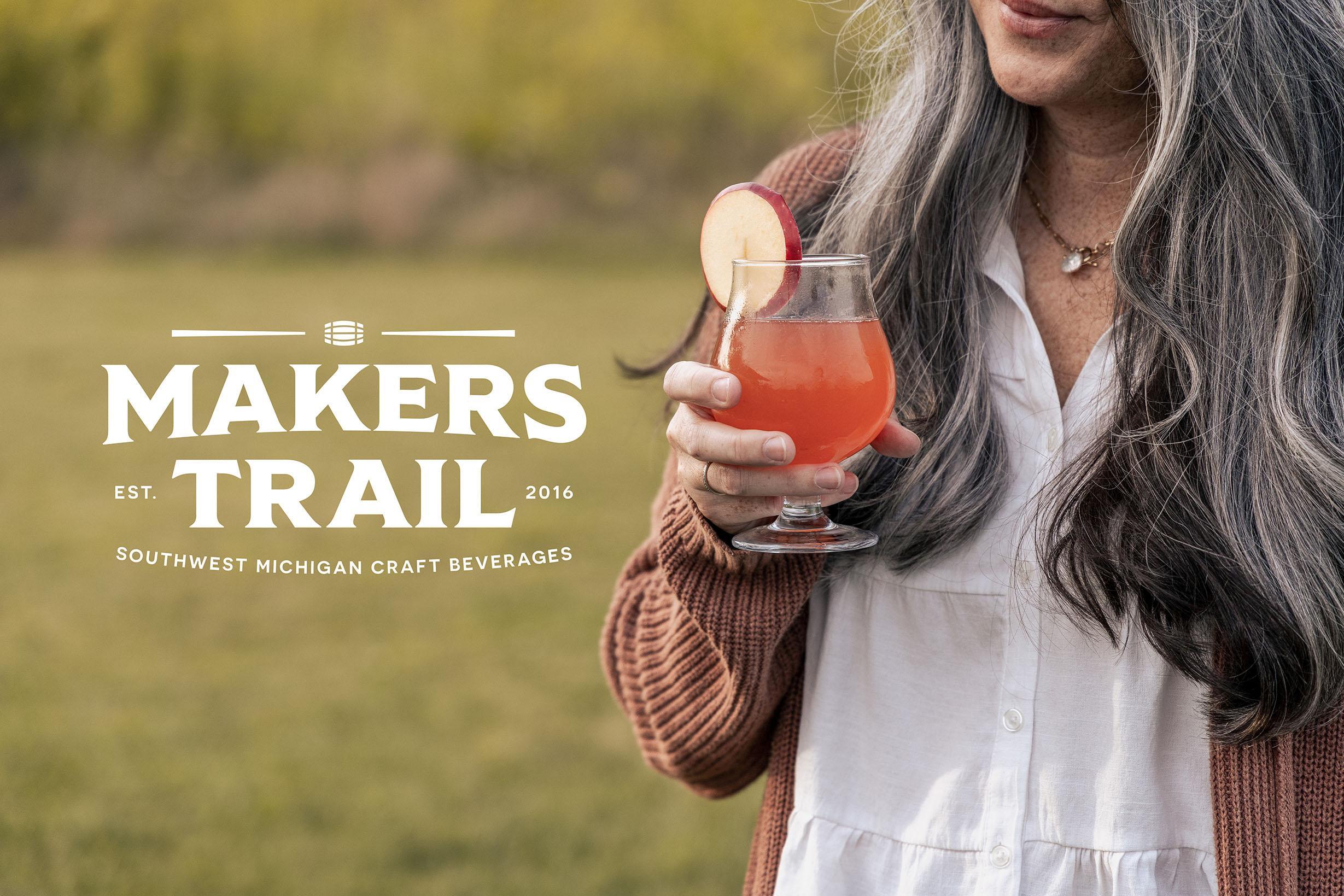 A person enjoys a craft beverage outdoors alongside the Makers Trail logo.