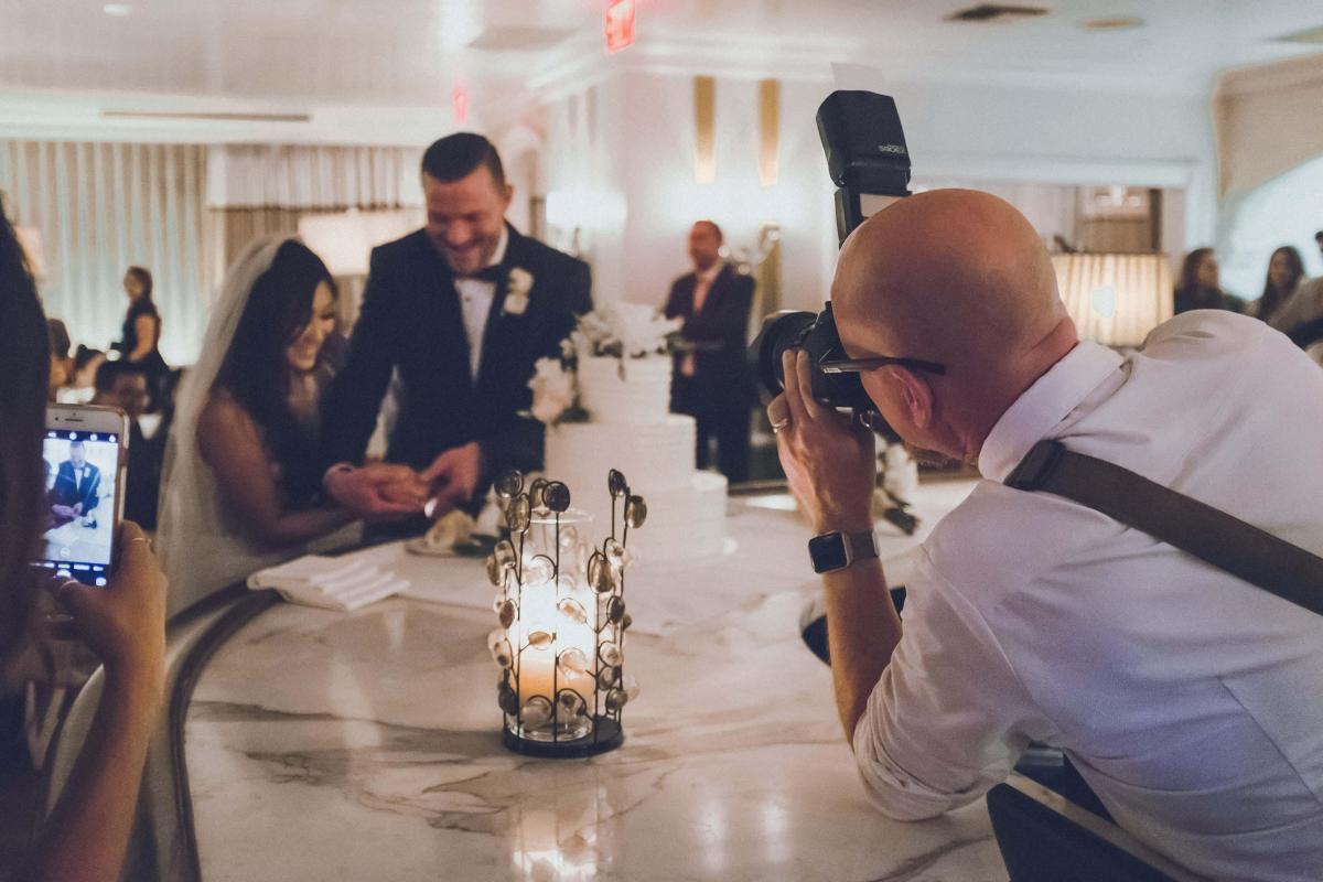 A wedding photographer captures the bride and groom cutting the cake.