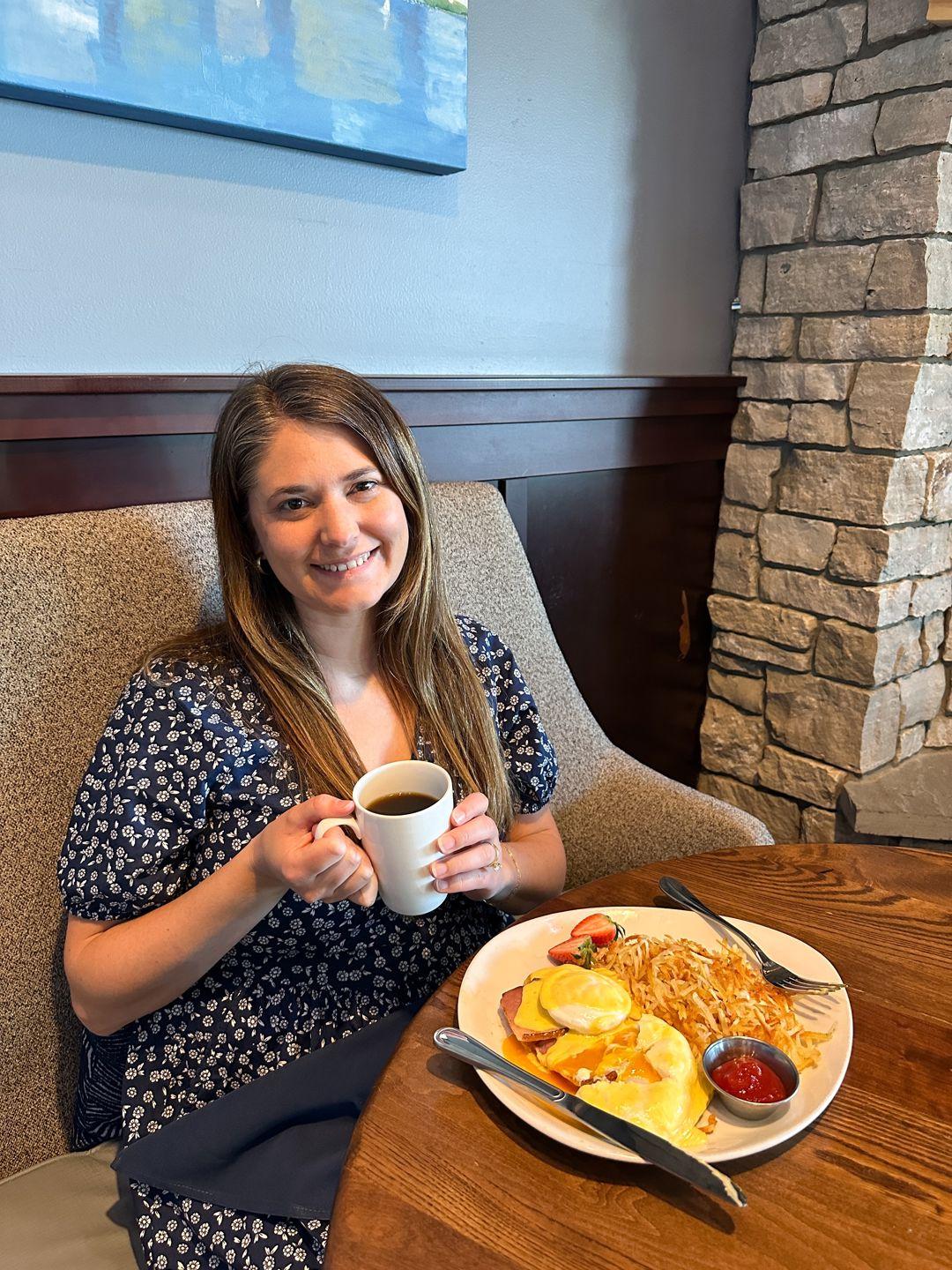A person sits at a table posing with a cup of coffee and a plate of food at Plank's Tavern on the Water.
