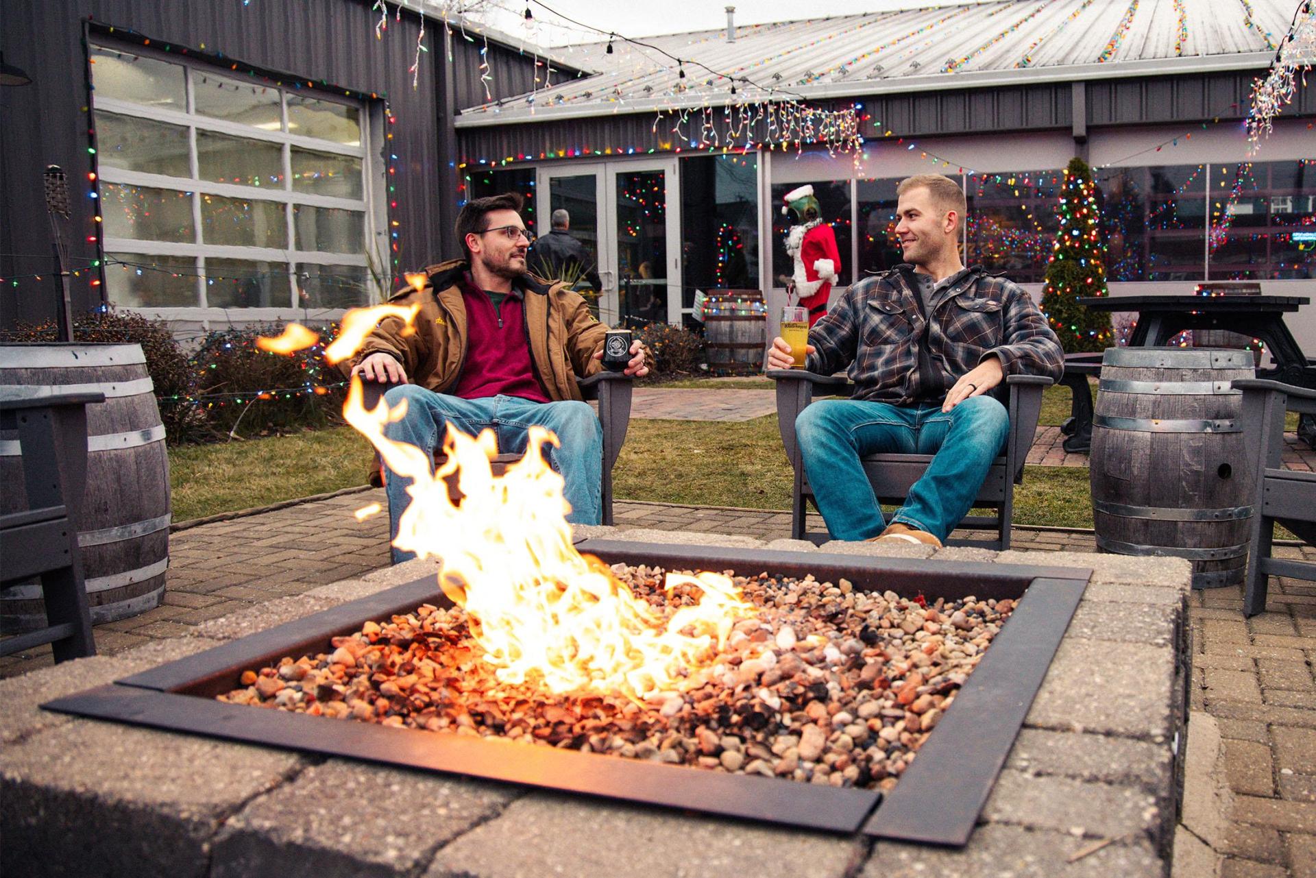 Two people relax with drinks by a fire outside at Watermark Brewery.