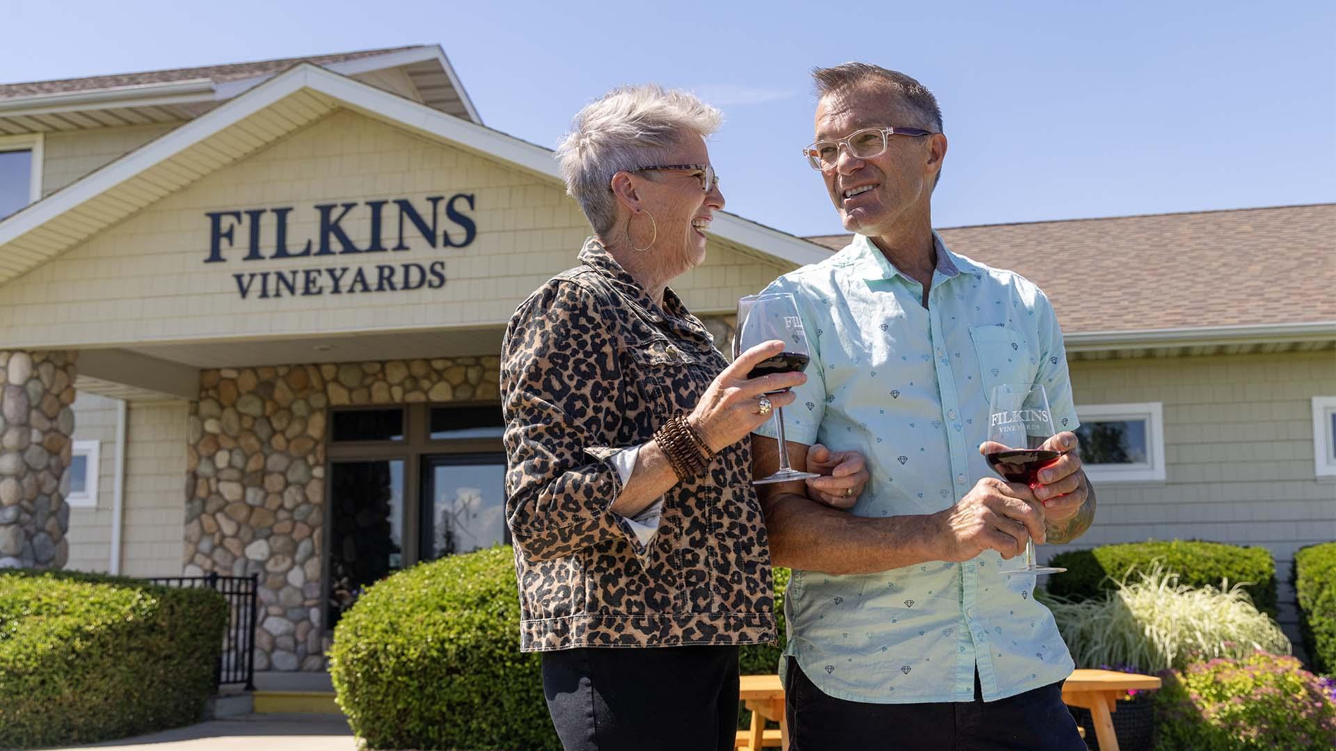 Two people holding glasses of wine outdoors at Filkins Vineyards.