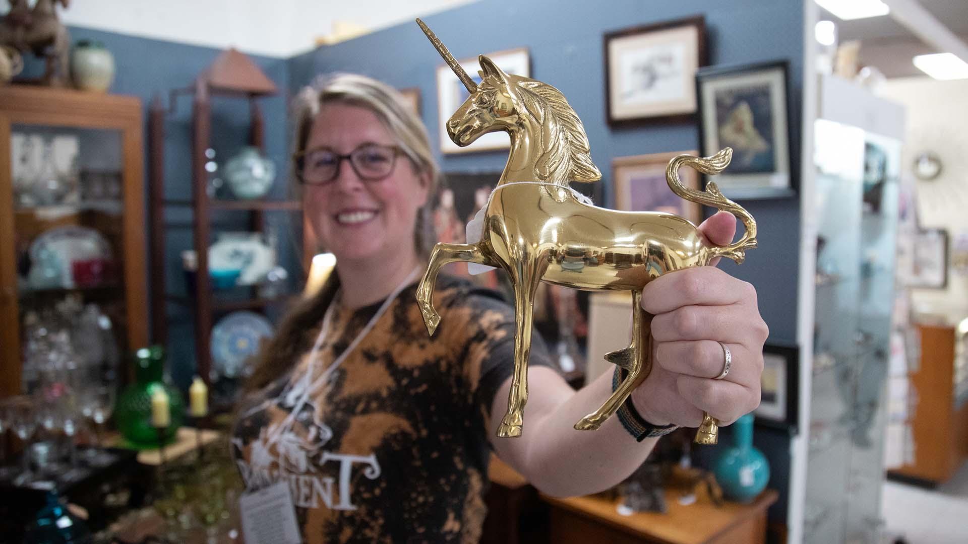 A person holding a small antique brass unicorn figurine inside an antique shop.
