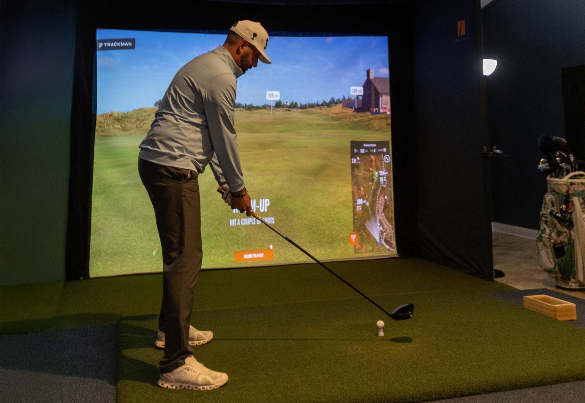A golfer practices a shot in a TrackMan-powered simulator bay at The Depths Society Golf.