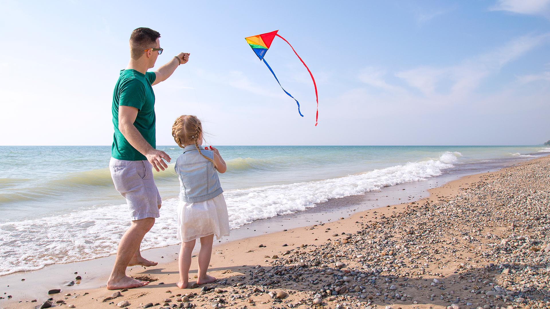 A father helping his young daughter fly a kite on the beach, with Lake Michigan and a clear_Ufjk