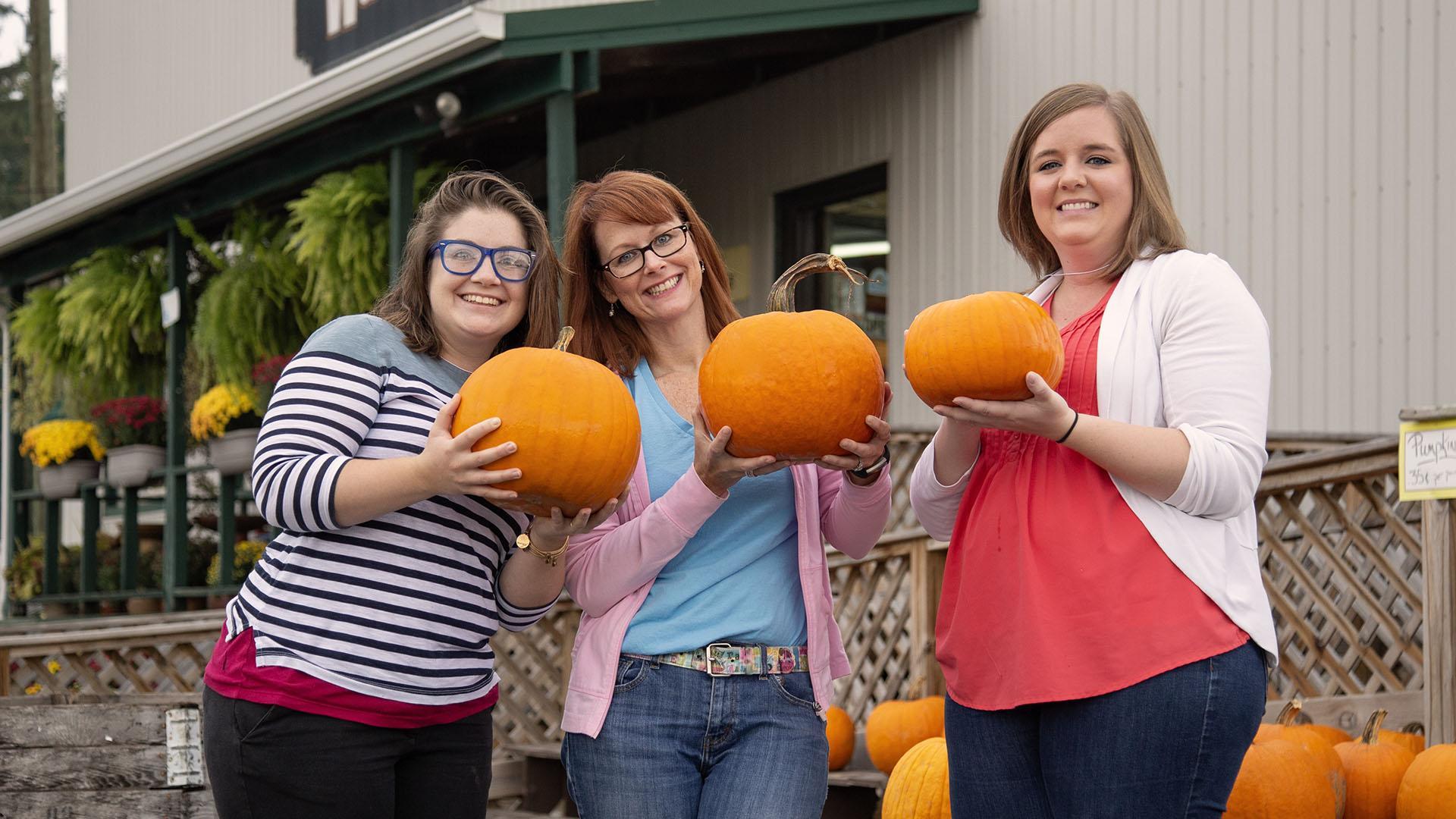 Three people holding pumpkins